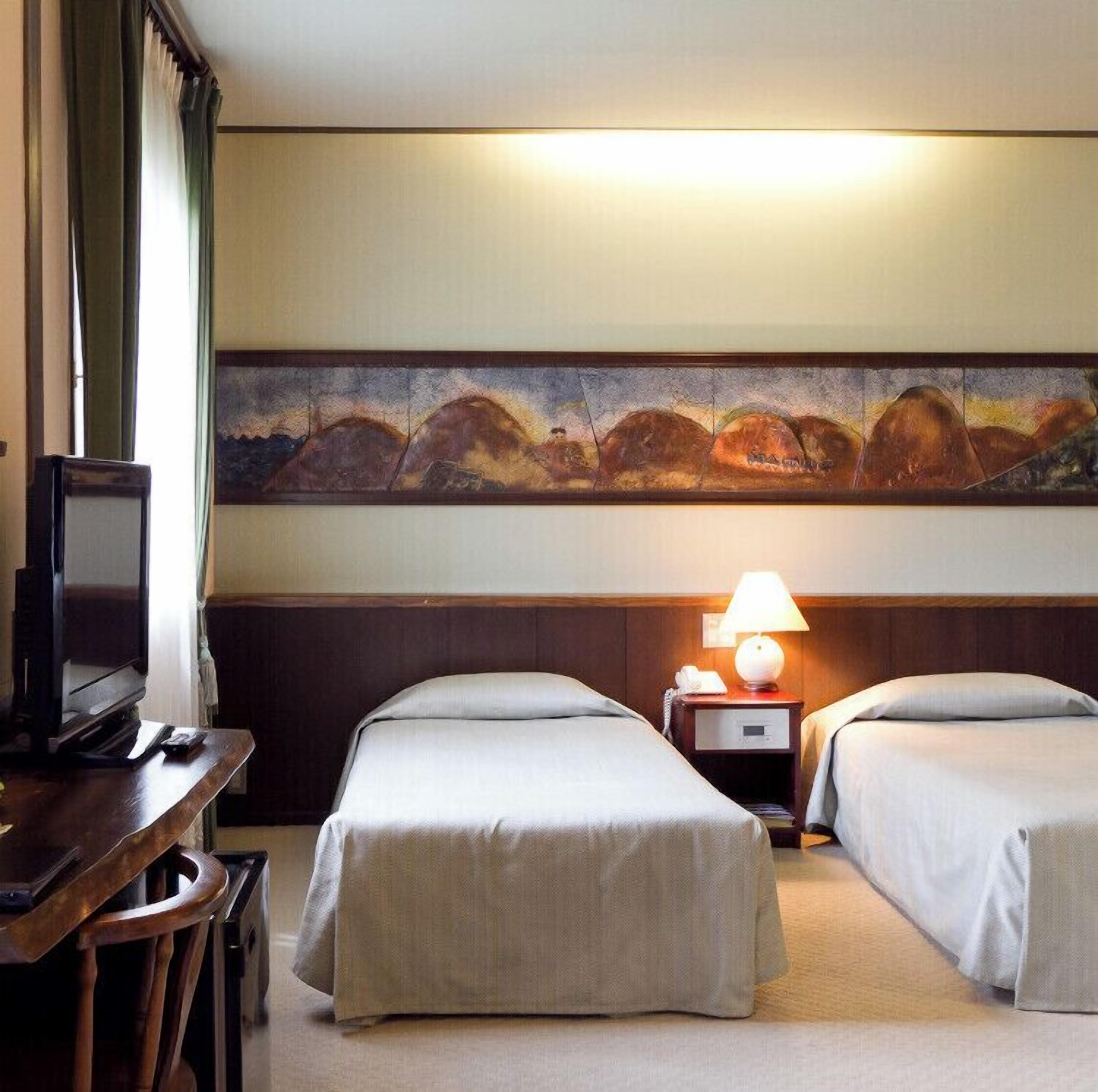 Habitación de hotel con dos camas, un televisor, un cuadro en la pared y una lámpara en la mesita de noche.