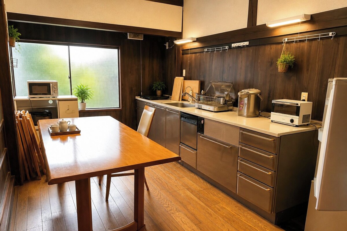 Een moderne keuken met houten vloeren, roestvrijstalen apparatuur, een eettafel met stoelen en een raam met uitzicht op groen.