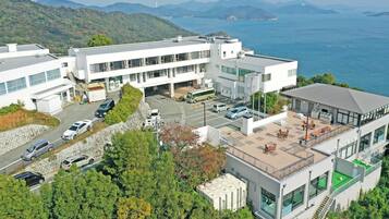 A modern building with a rooftop terrace, parking area, and a view of the sea.