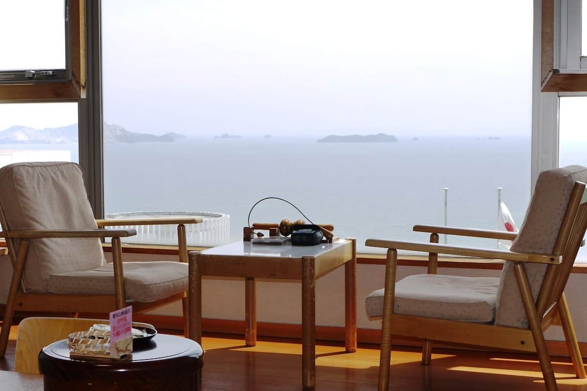 Una habitación con dos sillas de madera, una mesita y vista al mar a través de amplios ventanales.