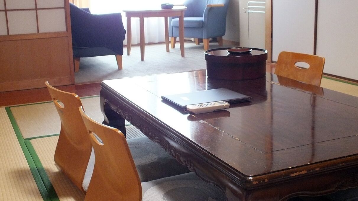 A traditional Japanese-style room with tatami flooring, a dark wooden table, and wooden chairs.
