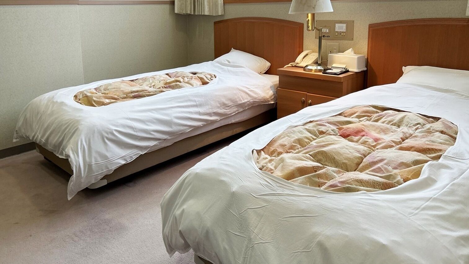 Two single beds with white linens, a bedside table with a lamp, and a nightstand with a phone and a tissue box.