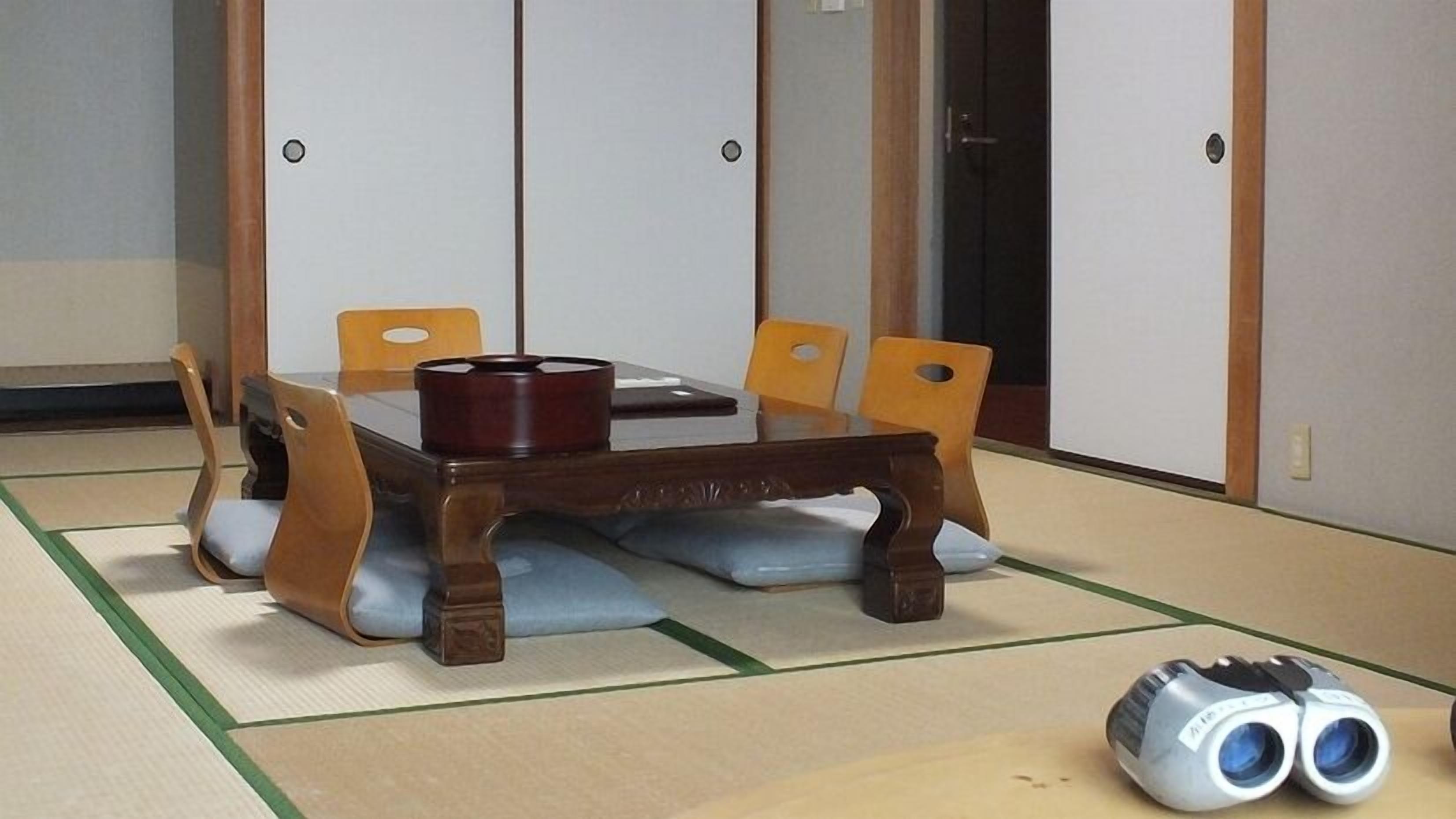 A traditional Japanese tatami mat room with a wooden table, four chairs, and a pair of binoculars on the floor.