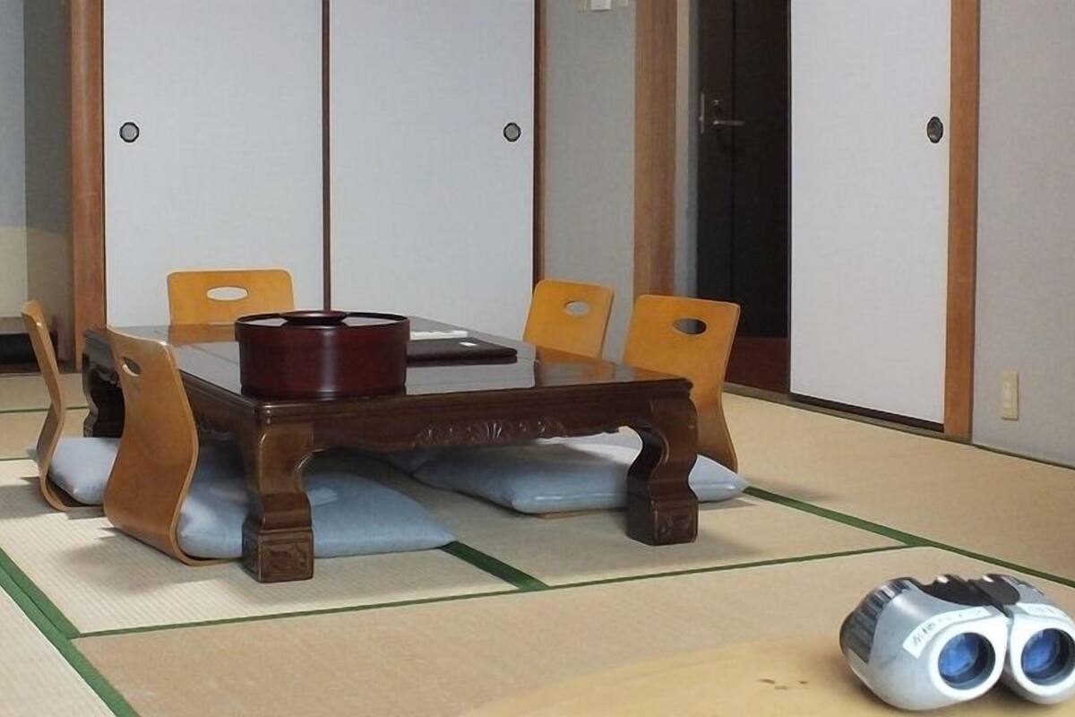 Una habitación tradicional japonesa con tatami, una mesa de madera, cuatro sillas y un par de binoculares en el suelo.