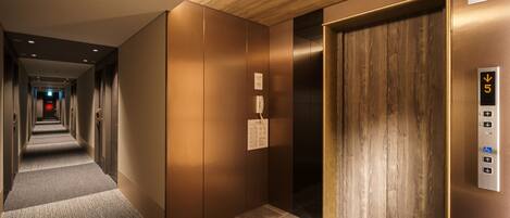 A modern elevator with a digital display, a wooden panel design, and a carpeted hallway leading to it.