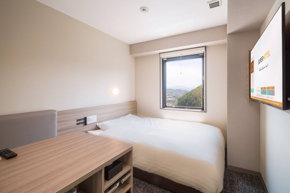 Een hotelkamer met een bed, een bureau, een televisie en een raam met uitzicht over de stad.