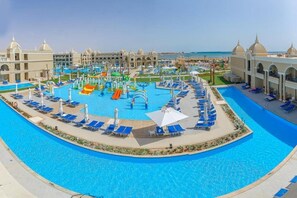 A large swimming pool with multiple lanes, surrounded by lounge chairs and umbrellas, and a water park area with slides and play structures. - Titanic Royal (Hurghada)