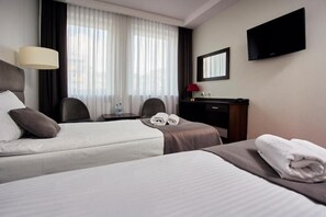 A hotel room with two beds, a desk, a chair, a TV, and a window with curtains. - Hotel Maraton (Bydgoszcz)