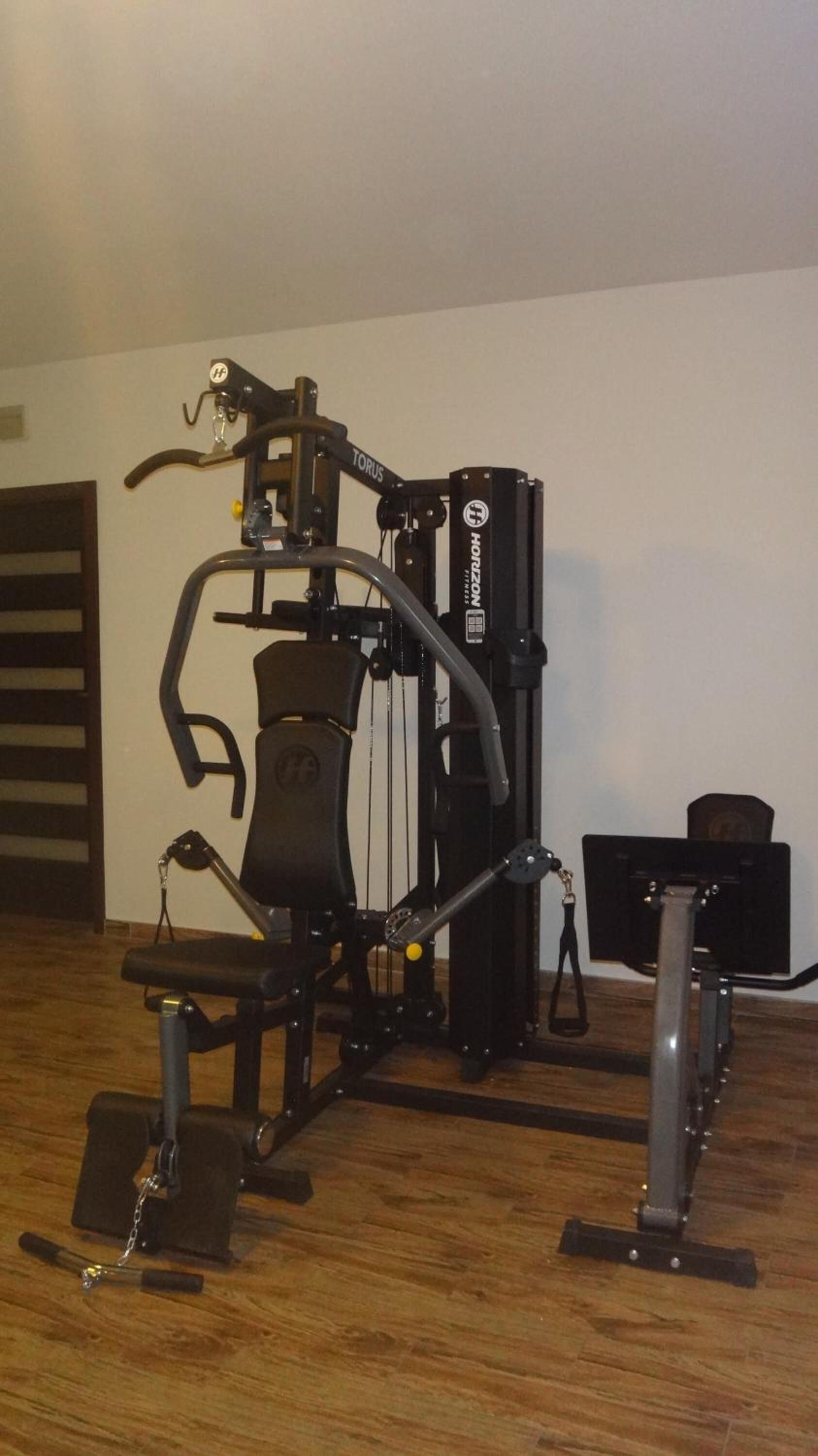 Un gimnasio en casa con barra de dominadas, máquina de press de banca y máquina de press de piernas.