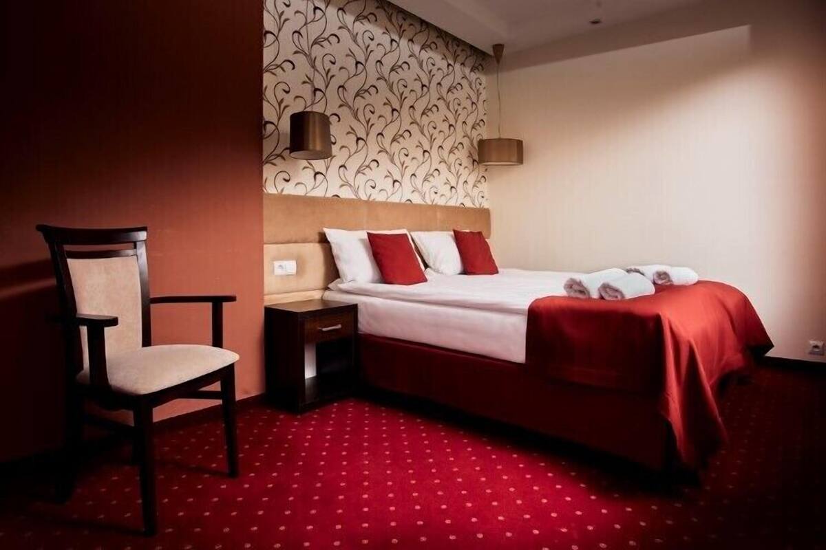 Hotellihuone, jossa on sänky, tuoli, yöpöytä ja kuviollinen tapetti.