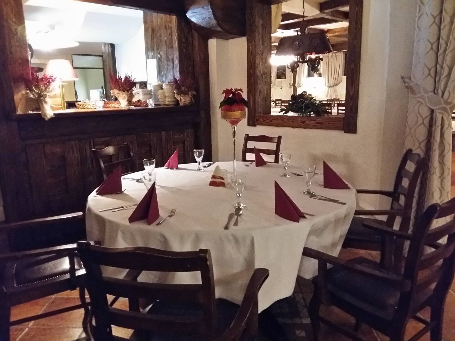 Mesa redonda de comedor con mantel blanco, servilletas rojas y cubiertos.