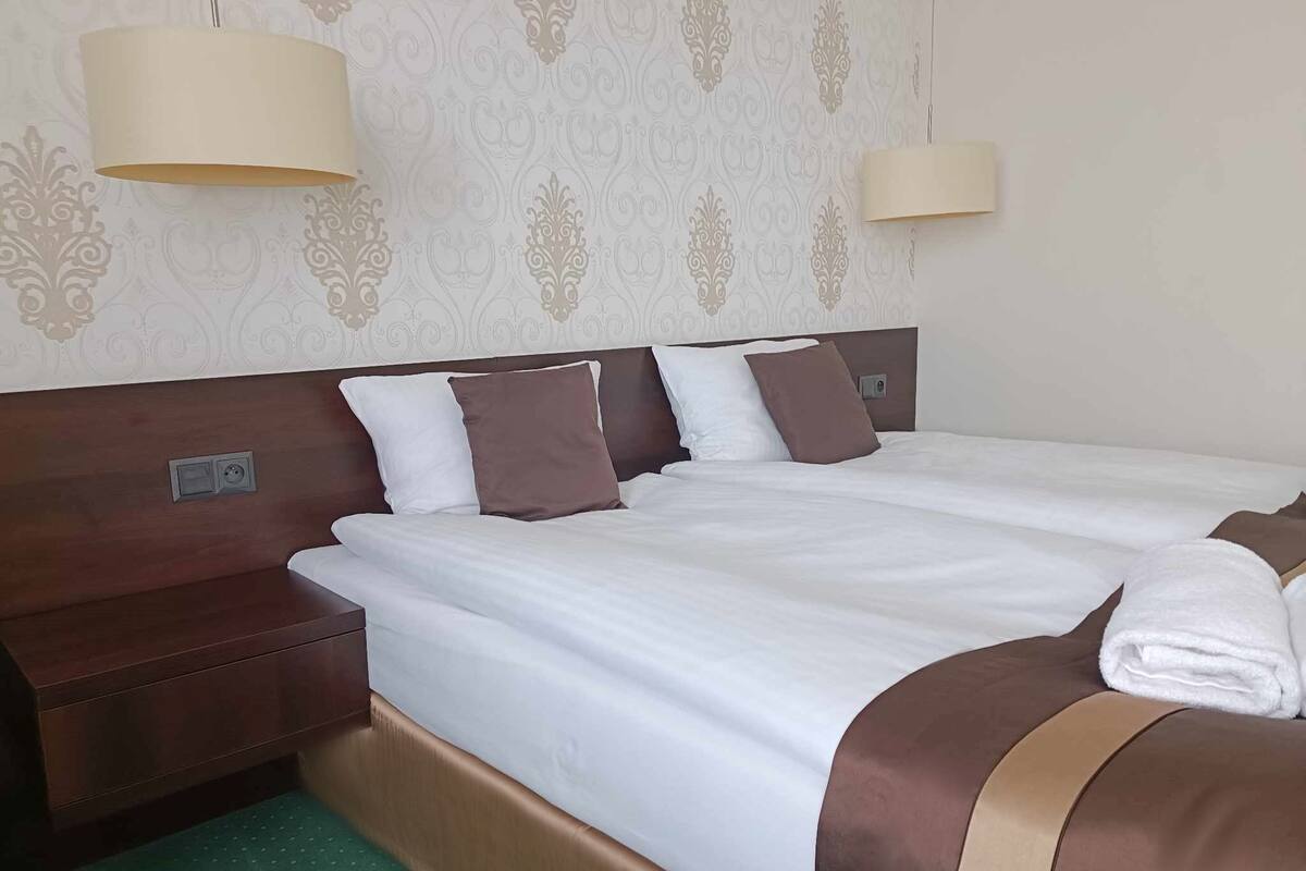 Hotellihuone, jossa on parivuode, kaksi tyynyä, yöpöytä ja lamppu.