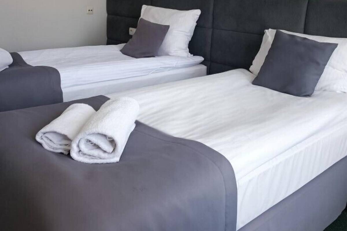 Hotellihuone, jossa on kaksi erillistä sänkyä. Jokaisessa sängyssä on harmaa pääty, valkoiset vuodevaatteet ja valkoinen pyyhe, joka on taiteltu sängyn päälle.