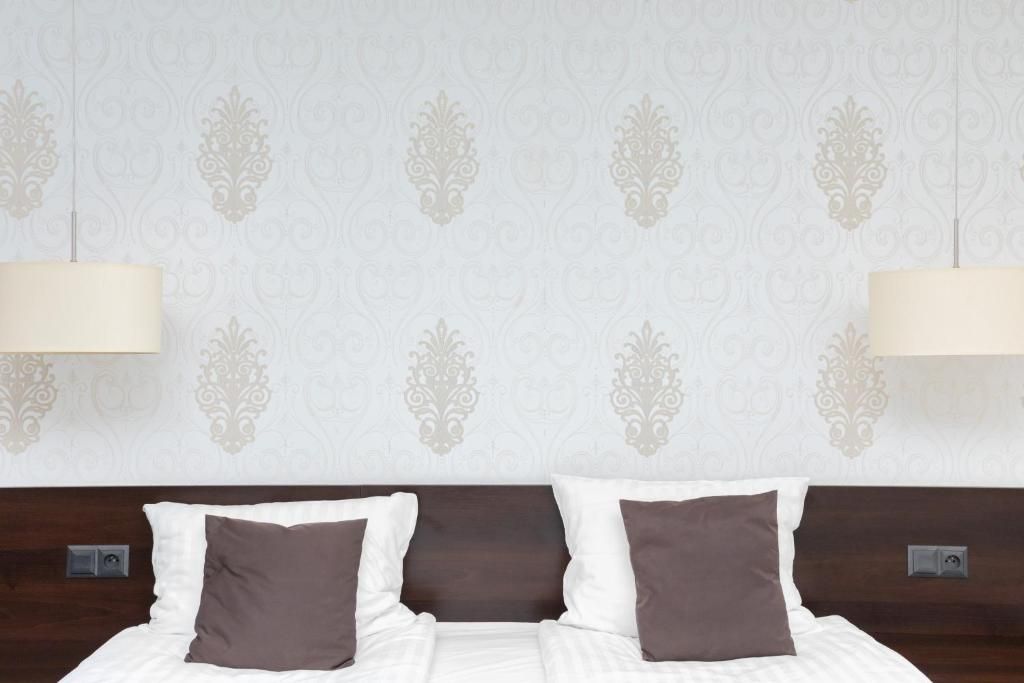 A hotel room with a bed, two bedside lamps, and a patterned wallpaper.