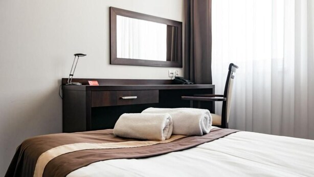 Una habitación de hotel con cama, escritorio, silla, espejo y ventana con cortinas.