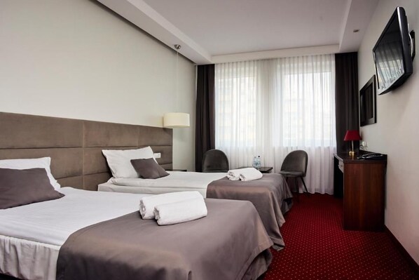 A hotel room with two beds, a desk, a chair, a TV, and a red carpet. - Hotel Maraton (Bydgoszcz)