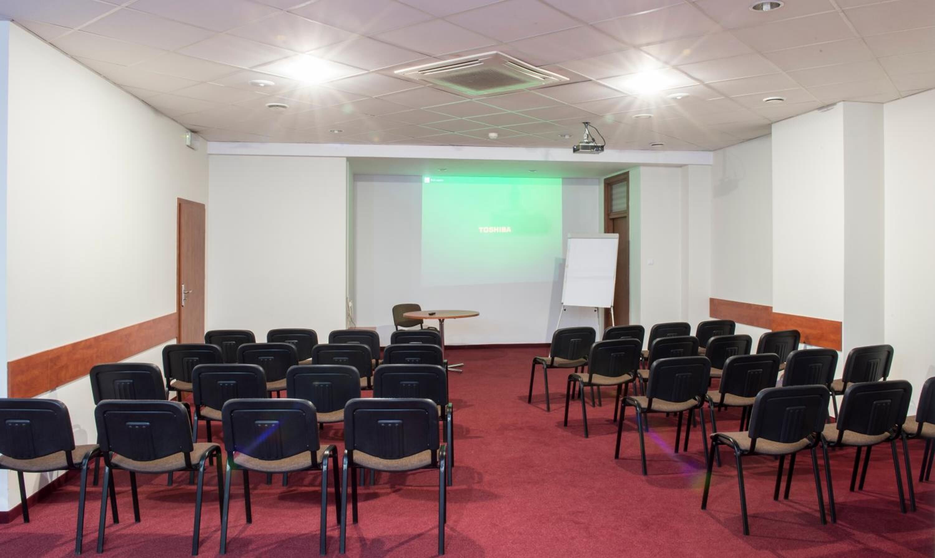 Un salón de conferencias con filas de sillas, una pantalla de proyector y una pizarra.