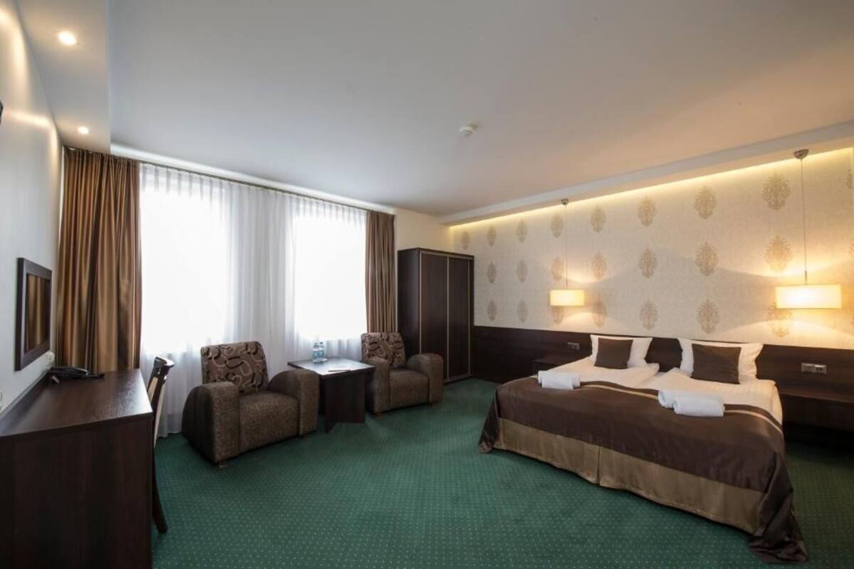 Hotellihuone, jossa on suuri sänky, kaksi nojatuolia, työpöytä ja vaatekaappi.