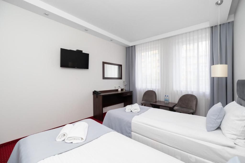 Habitación de hotel con dos camas, un escritorio, una silla, un televisor y una ventana con cortinas.