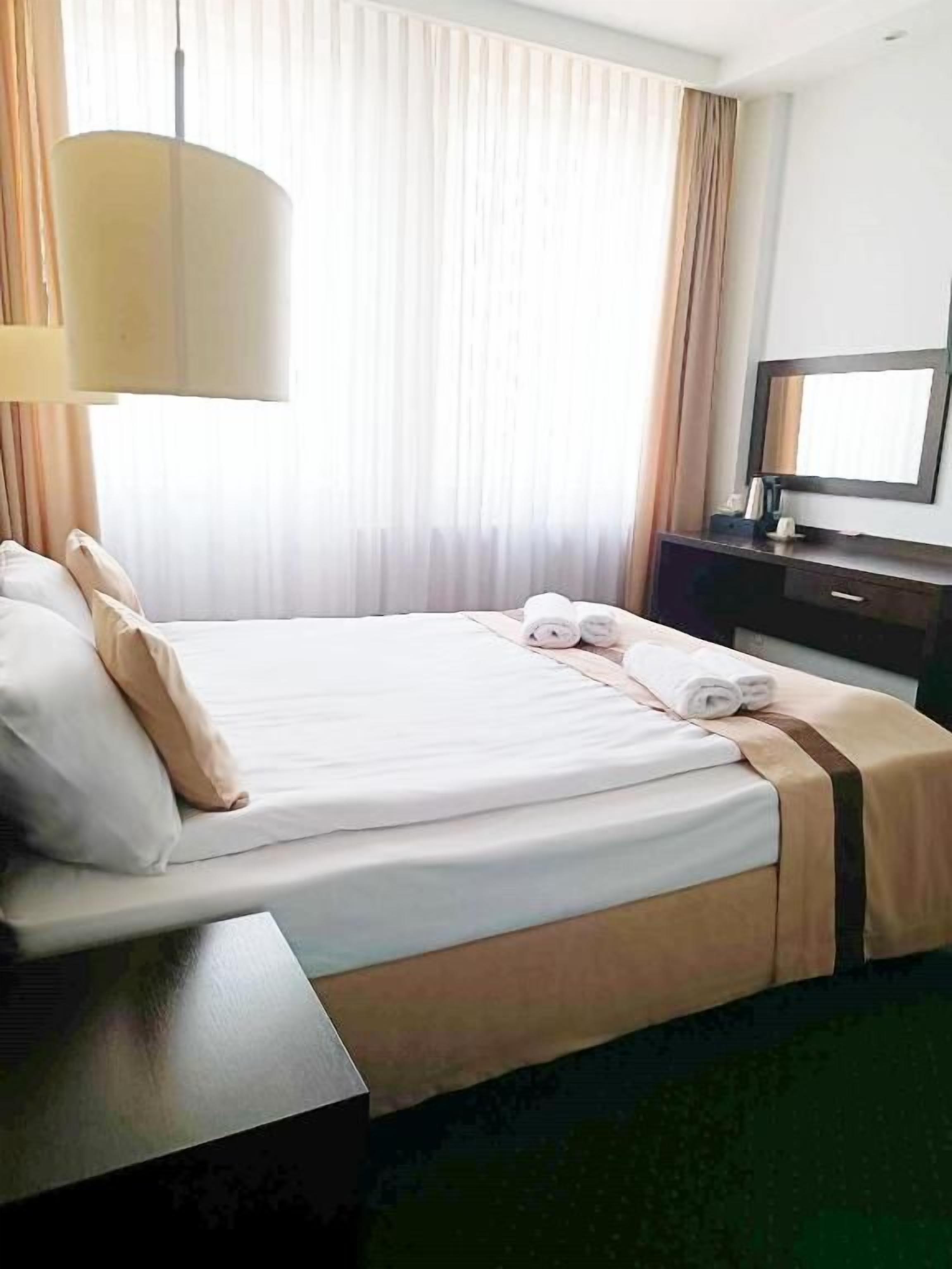 A hotel room with a bed, a desk, a lamp, a television, and a window with curtains.