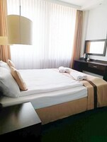 Habitación de hotel con cama, escritorio, lámpara, televisor y ventana con cortinas.