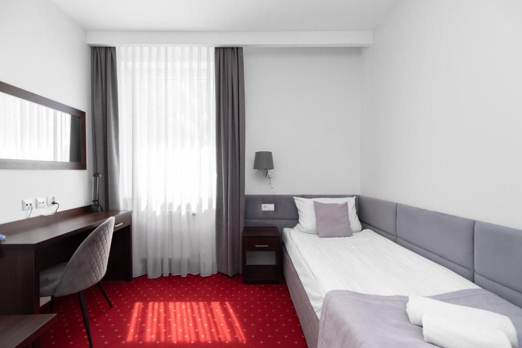 Habitación de hotel con una cama, un escritorio, una silla, una mesita de noche y una lámpara.