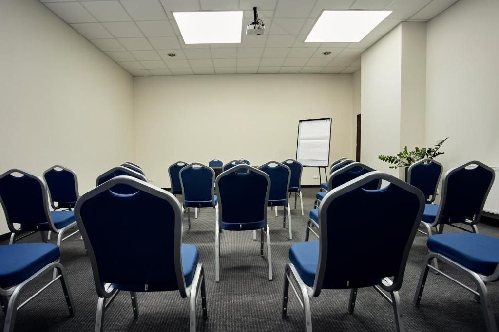 Un salón de conferencias con filas de sillas azules, una pizarra y un proyector en el techo.