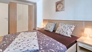 A bedroom with a bed, two nightstands, a wooden headboard, a painting, and a wardrobe.