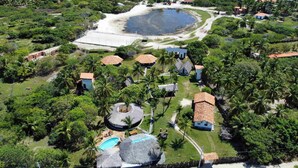 An aerial view of a resort with multiple thatched-roof structures, a swimming pool, and a large body of water. - Le Marin Hotel Boutique (Barreirinhas)