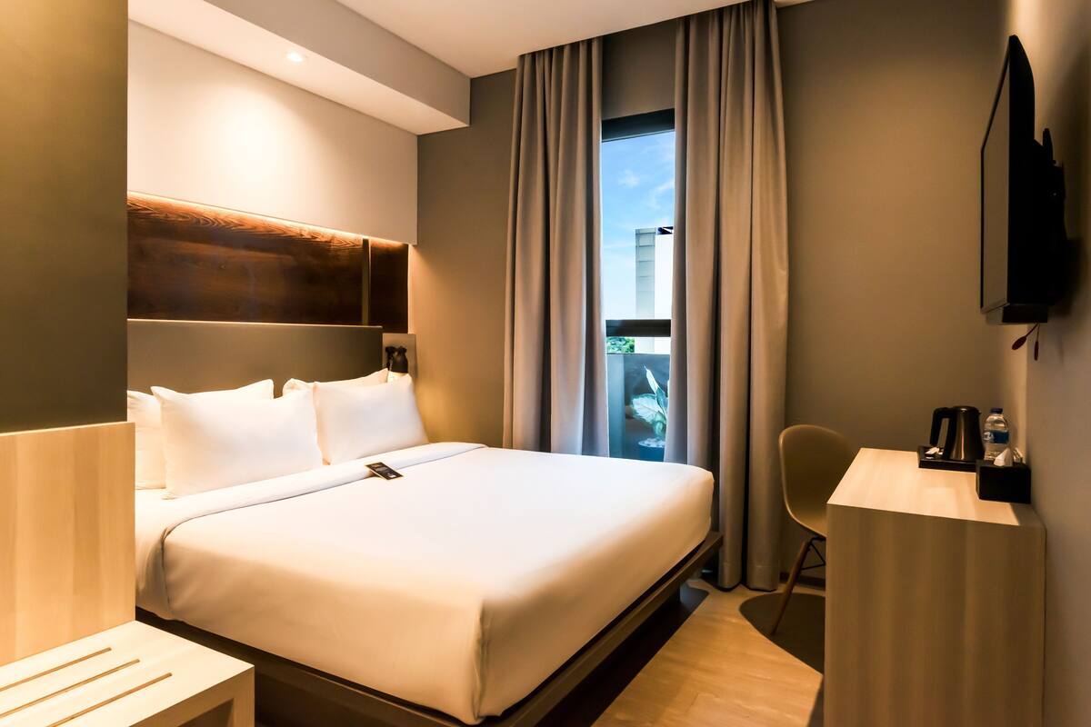 Une chambre d’hôtel avec un lit, un bureau, une chaise, une télévision et une fenêtre avec des rideaux.