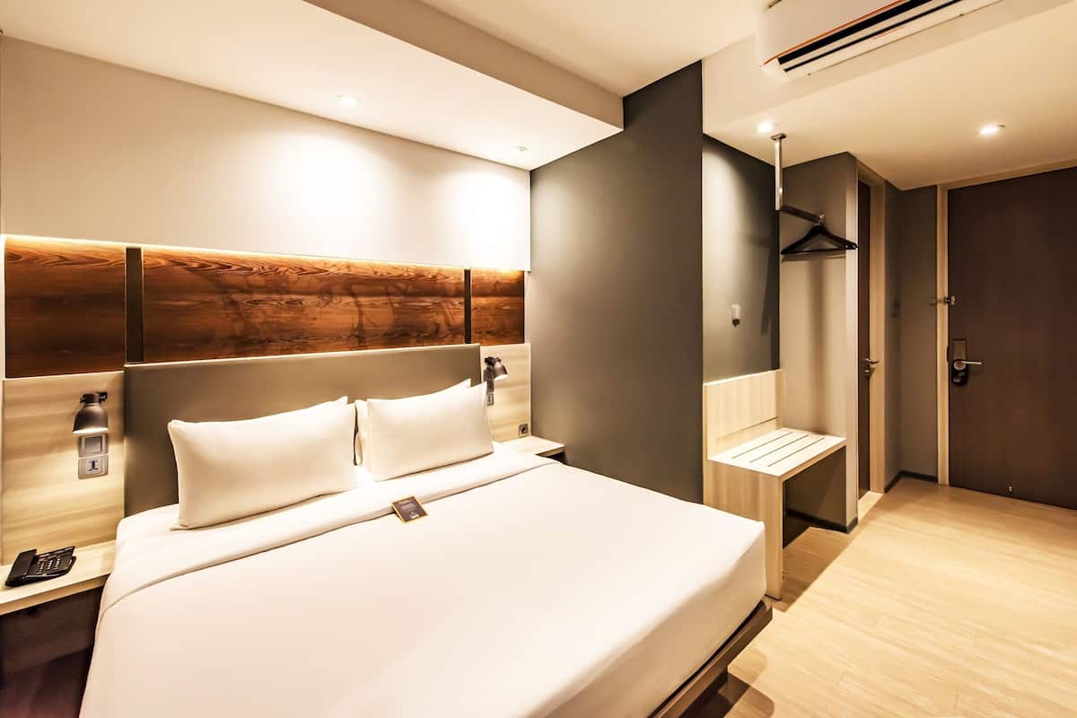 Une chambre d’hôtel moderne avec un grand lit, une table de chevet et une tête de lit en bois.