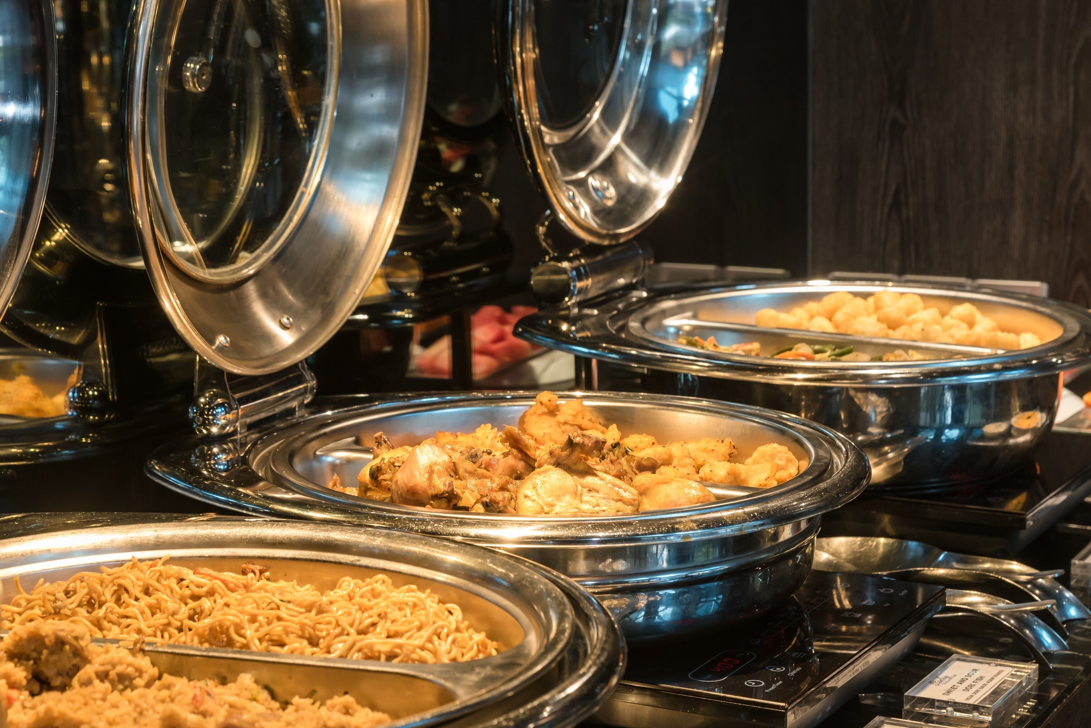 A buffet with various dishes in metal serving dishes, including noodles and fried items.