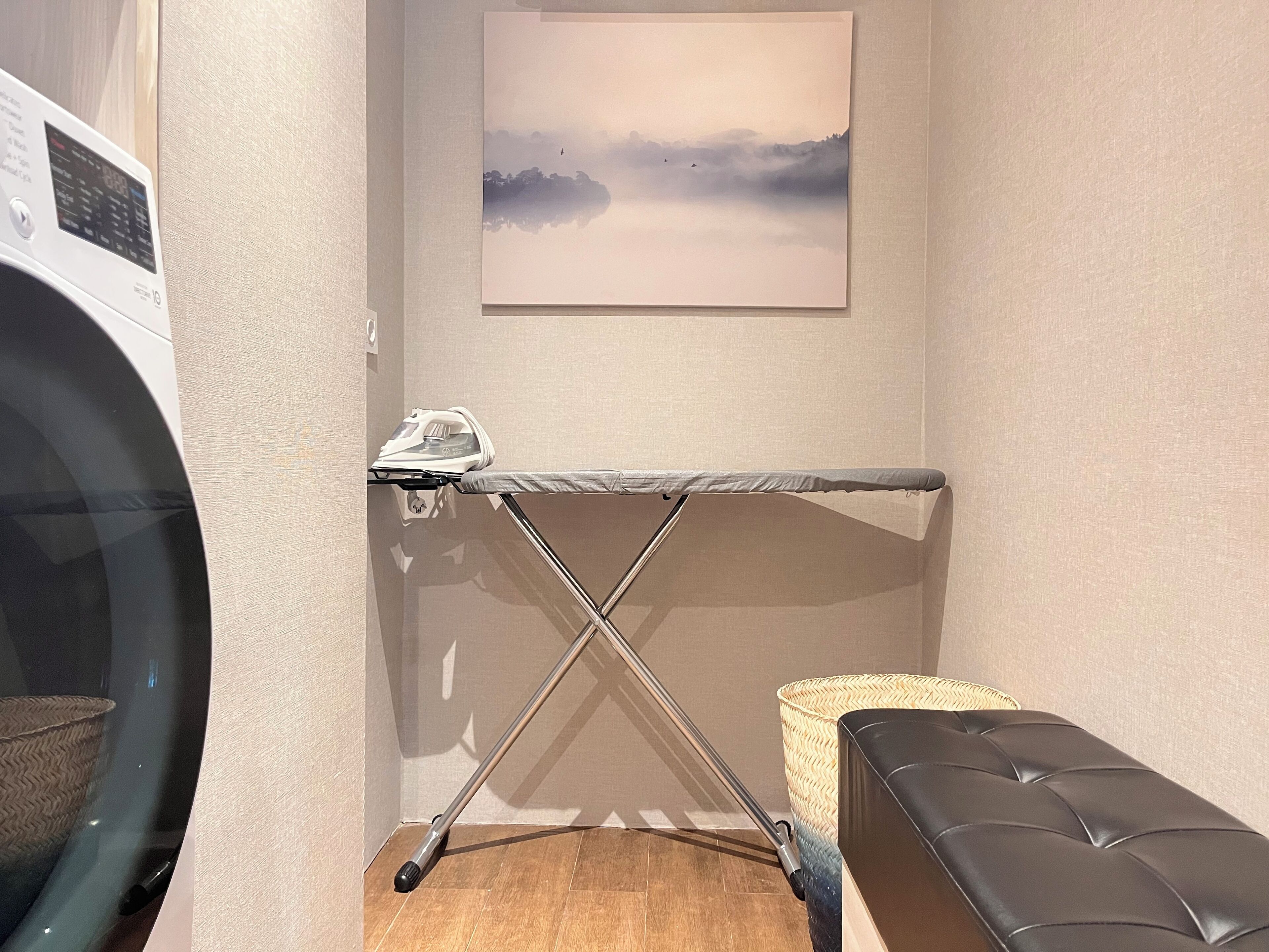 A laundry area with a washing machine, an ironing board, and a bench.
