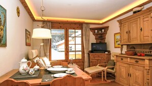 Un coin repas chaleureux avec une table en bois dressée pour quatre personnes, un téléviseur posé sur un meuble en bois et une fenêtre donnant sur un paysage enneigé.