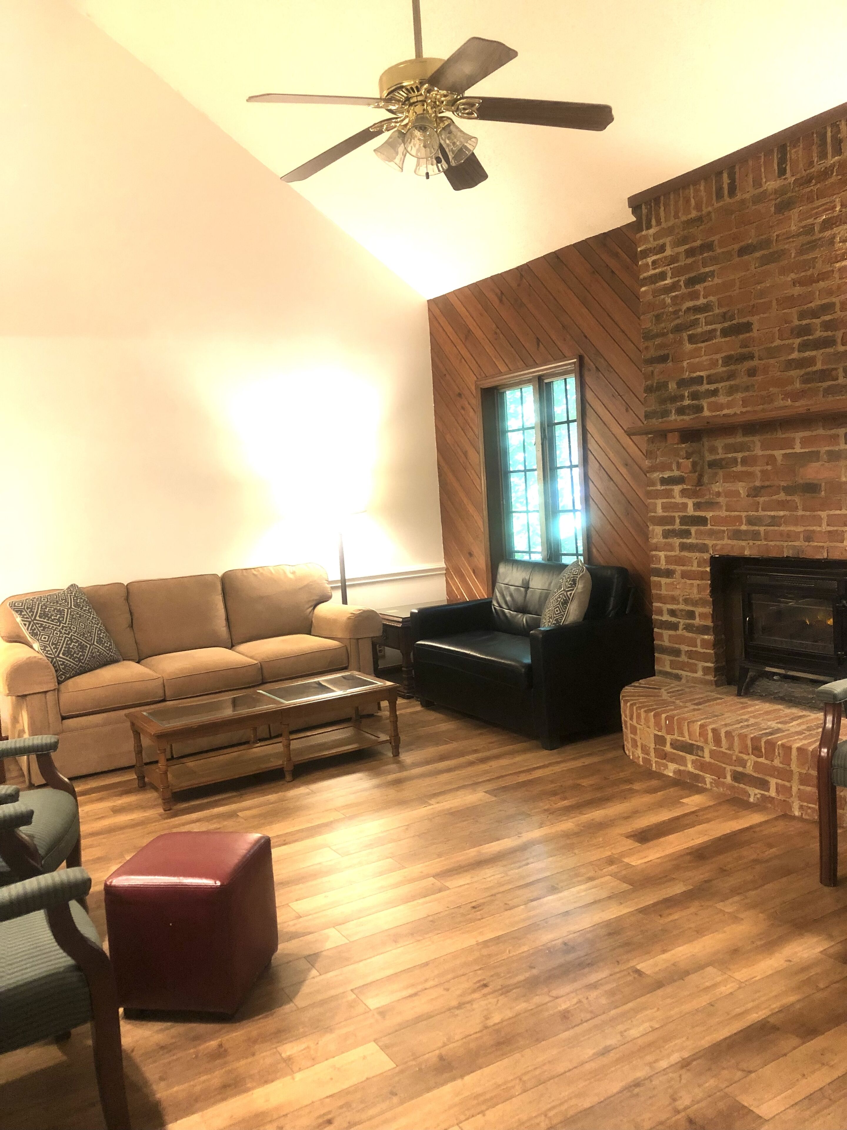 A living room with a wooden floor, a brick fireplace, a ceiling fan, and a sofa.