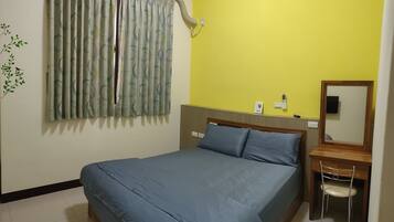 A bedroom with a bed, a desk, a chair, an air conditioner, and a mirror.