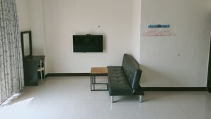 Una sala moderna con un sofá de cuero negro, una mesita de madera, un televisor de pantalla plana montado en la pared y un espejo sobre el sofá.