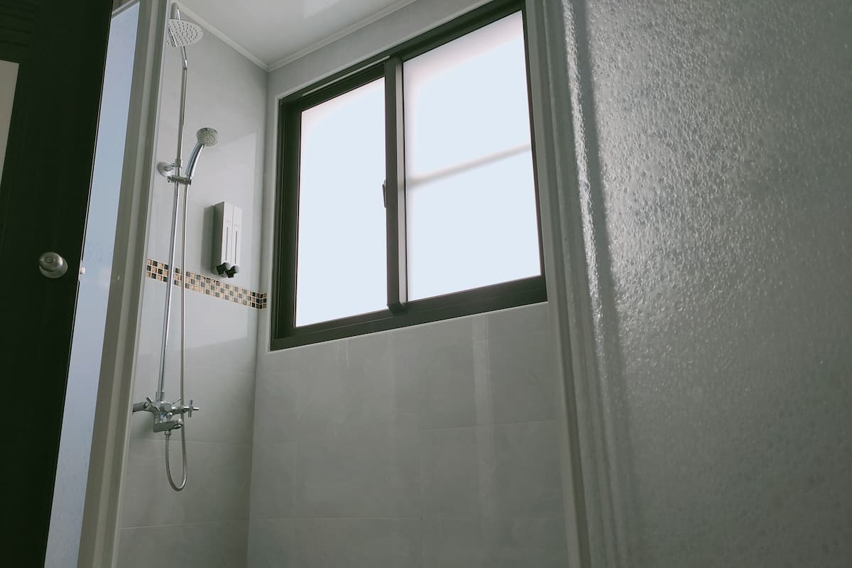 Un bagno con doccia, finestra e pareti in piastrelle.