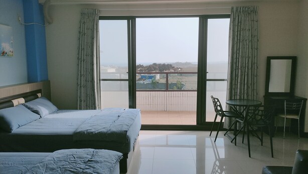 Habitación de hotel con dos camas, un balcón con vistas, una pequeña mesa y sillas, y un equipo de aire acondicionado.