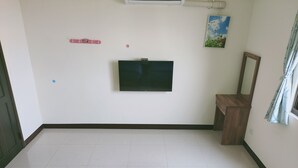 Una habitación con una televisión de pantalla plana montada en la pared, una pequeña mesa de madera, un espejo y una ventana con cortinas.