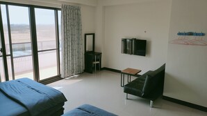 Habitación de hotel con un gran ventanal corredero, televisor de pantalla plana, una mesita, un sofá y una cama.
