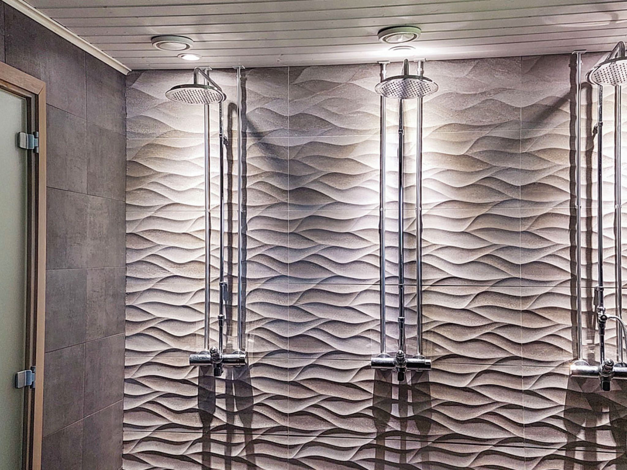 Un baño con pared texturizada y tres duchas superiores.