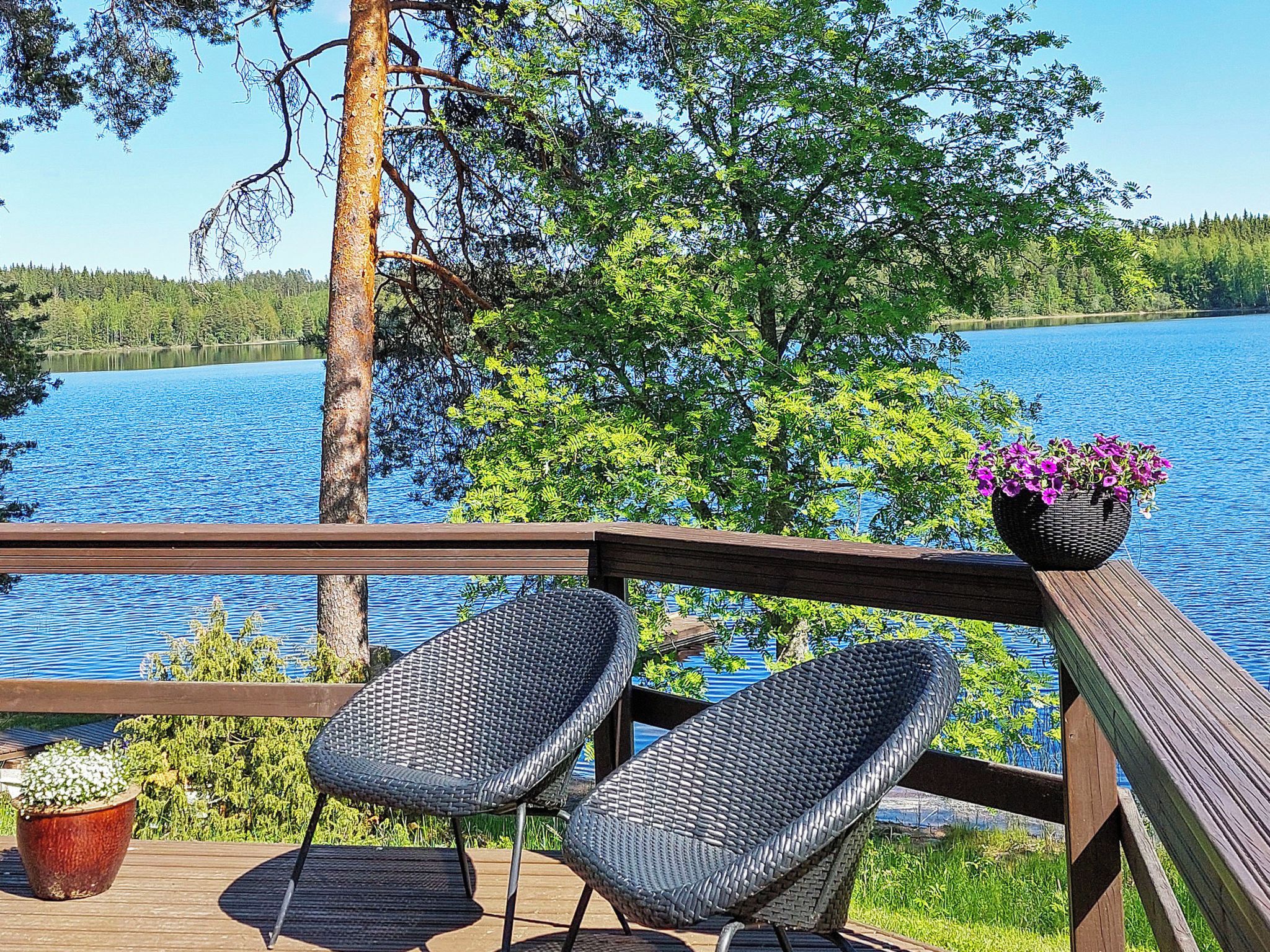 Une terrasse en bois avec deux fauteuils en osier et une plante en pot.