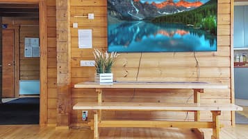 A wooden interior with a wooden bench, a wall-mounted TV displaying a mountain lake, and a small plant on the bench.
