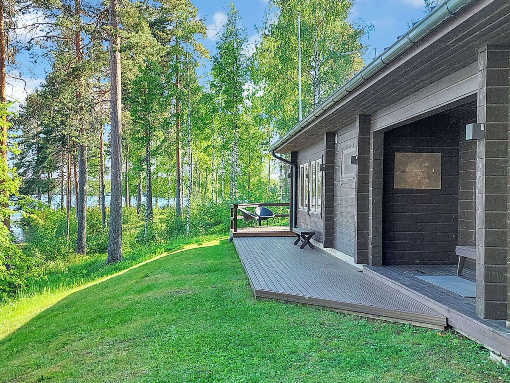 Une cabane moderne dotée d’une terrasse offrant une vue sur une zone boisée et un plan d’eau.