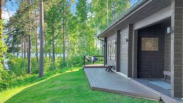 Une cabane moderne dotée d’une terrasse offrant une vue sur une zone boisée et un plan d’eau.