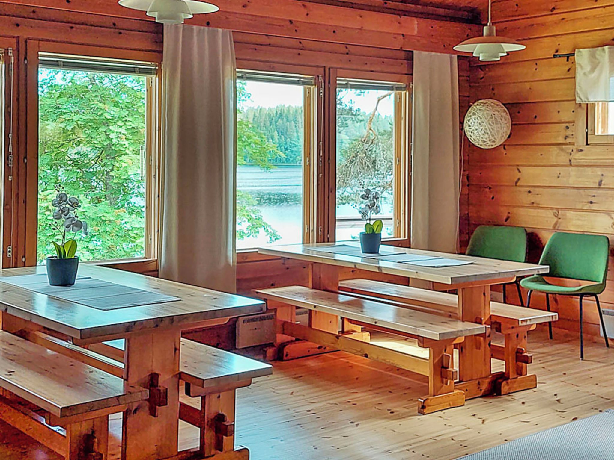 A wooden cabin interior with large windows, wooden benches, and a green chair.