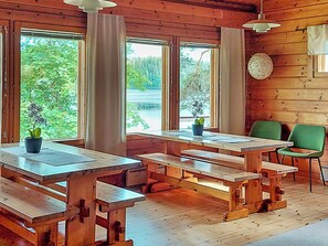 A wooden cabin interior with large windows, wooden benches, and a green chair.