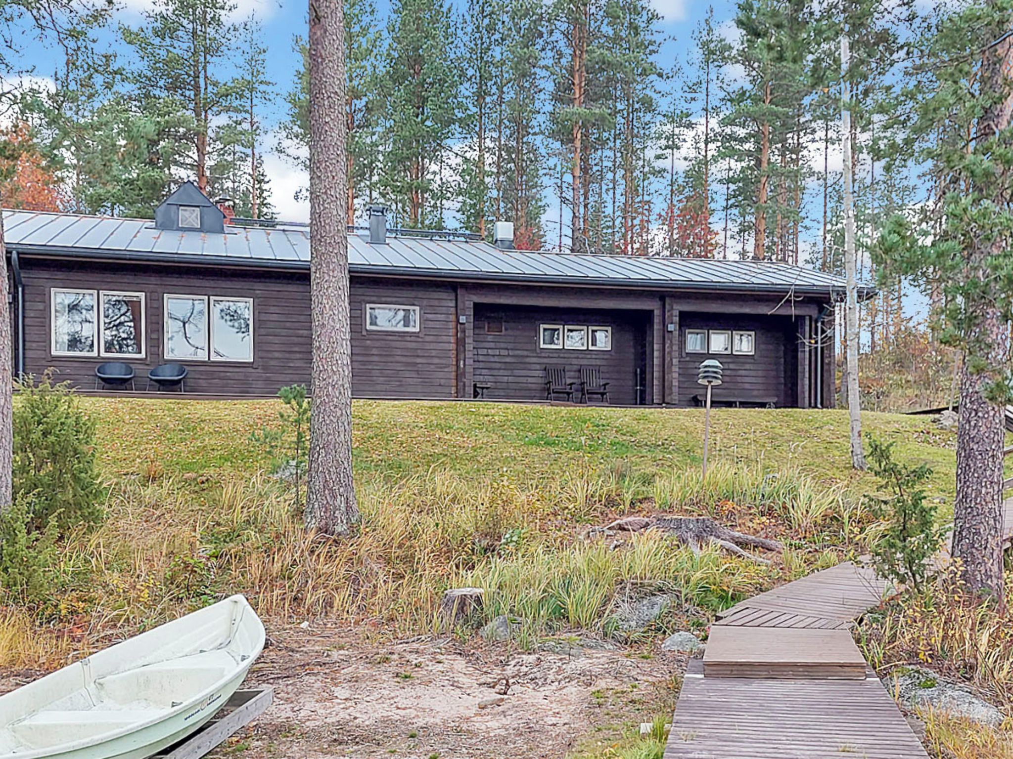 A cabin with a metal roof, two visible windows, and a dock with a boat.