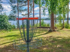 Een frisbeebaasket met kettingdoel, omringd door gras en bomen, met een meer en bergen op de achtergrond.